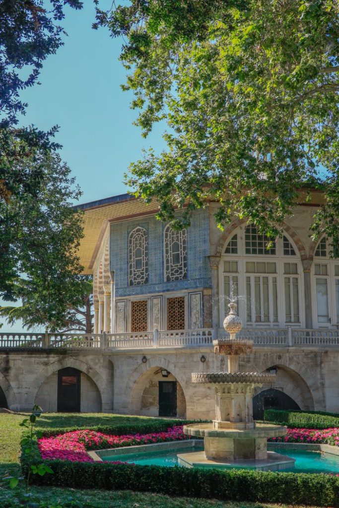 A serene scene of a historic mansion and ornate fountain in lush gardens.