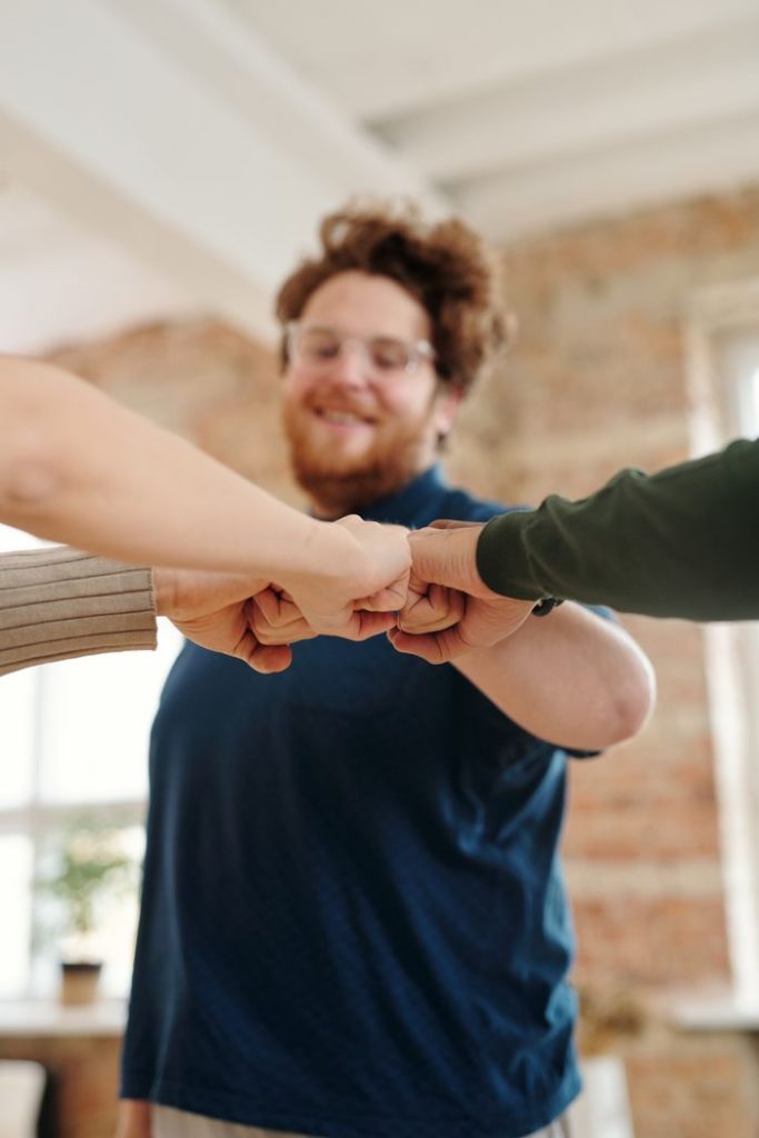 Group of diverse adults showing unity and teamwork with a fist bump indoors.
