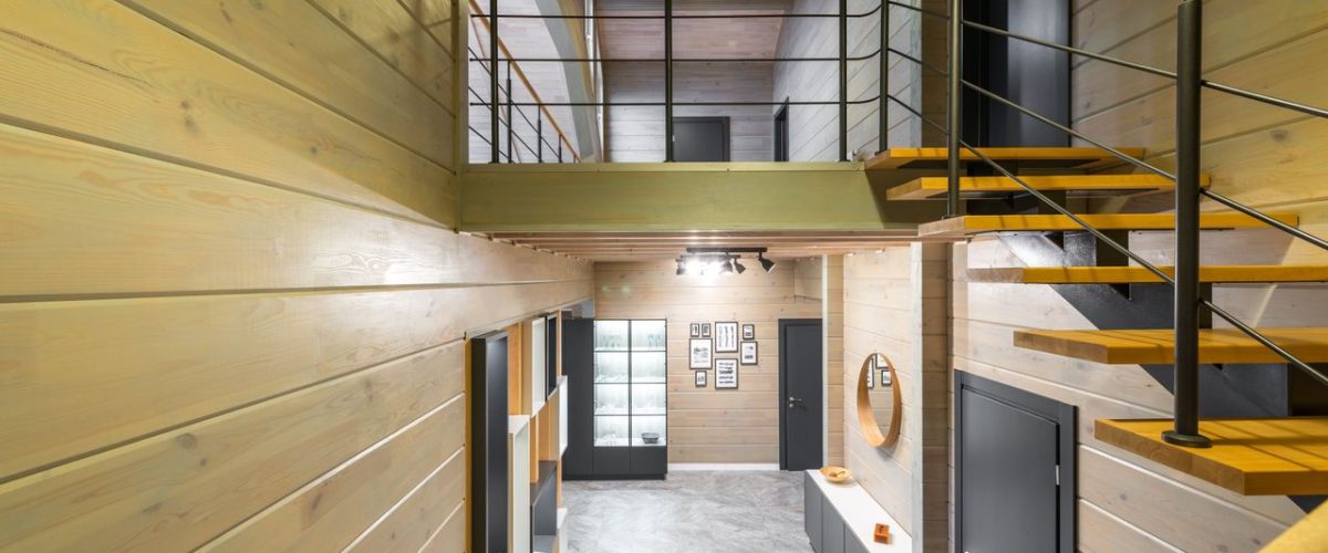Interior of spacious house with stairway leading to entry with door and mirror handing above cupboards
